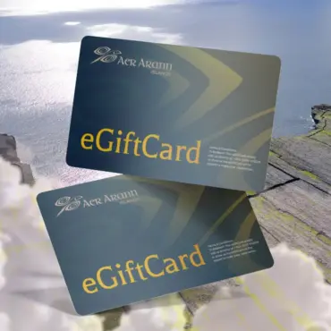Two Aer Arann Islands eGift Cards are shown overlapping on a scenic background of cliffs, clouds, and the ocean. These dark Aran Islands Gift Cards feature gold text and a logo in the upper left corner.