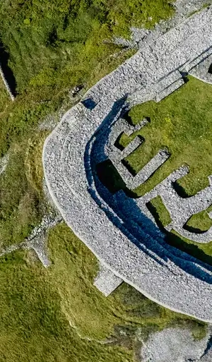 Aerial view of an ancient stone fort with circular walls and grassy interior, surrounded by green vegetation.