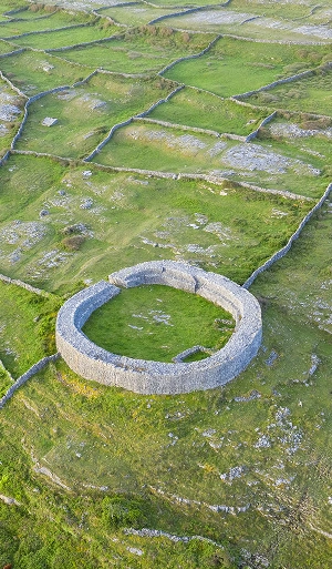 Aerial view of a large, circular ancient stone fort surrounded by green fields and stone walls in a rural landscape.