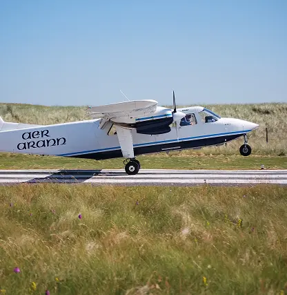 A small white Aer Arann plane is landing on a runway surrounded by grassy fields under a clear blue sky.